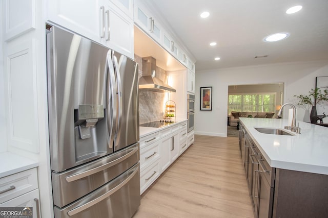 kitchen featuring white cabinets, a sink, stainless steel appliances, light countertops, and wall chimney exhaust hood