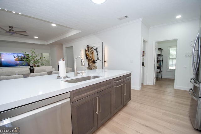 kitchen featuring crown molding, a sink, light wood-style floors, stainless steel appliances, and light countertops