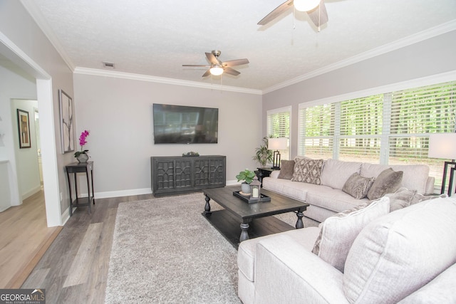 living room featuring ceiling fan, crown molding, visible vents, baseboards, and wood finished floors