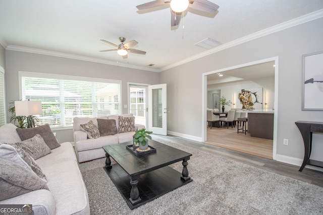 living room featuring a ceiling fan, visible vents, baseboards, ornamental molding, and wood finished floors