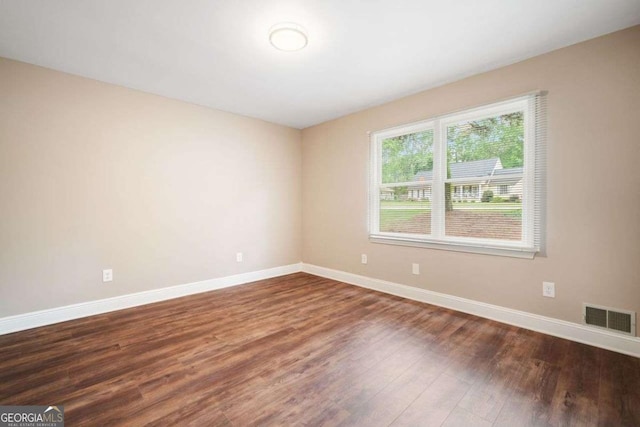 empty room with wood finished floors, visible vents, and baseboards