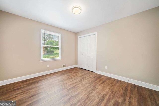 unfurnished bedroom featuring a closet, visible vents, wood finished floors, and baseboards