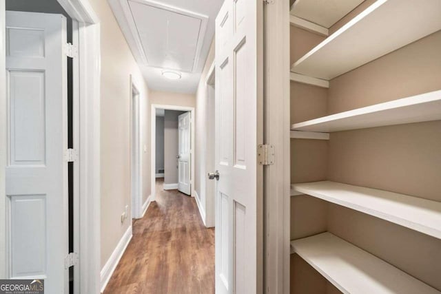 hallway featuring baseboards, attic access, and wood finished floors