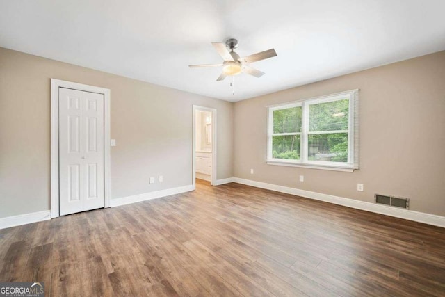 unfurnished bedroom featuring connected bathroom, visible vents, baseboards, wood finished floors, and a ceiling fan
