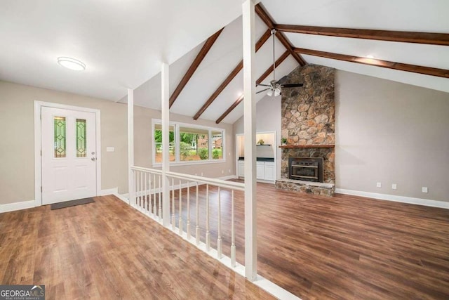 foyer entrance featuring beamed ceiling, a fireplace, a ceiling fan, baseboards, and wood finished floors