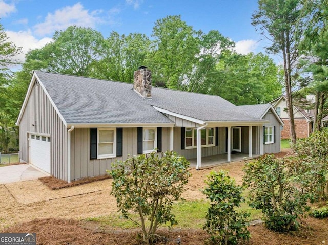 ranch-style home featuring a chimney, covered porch, driveway, roof with shingles, and an attached garage