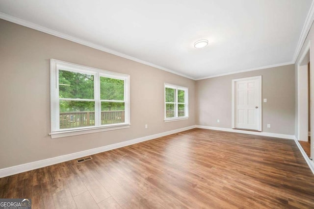 empty room featuring ornamental molding, visible vents, wood finished floors, and baseboards