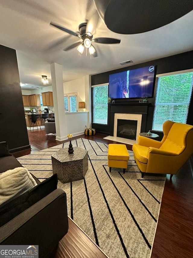 living area with a ceiling fan, visible vents, a fireplace with raised hearth, and wood finished floors