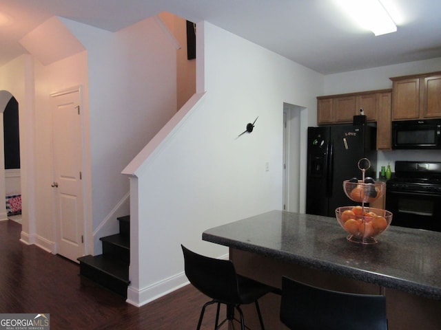 kitchen featuring arched walkways, dark wood-style flooring, black appliances, and dark countertops