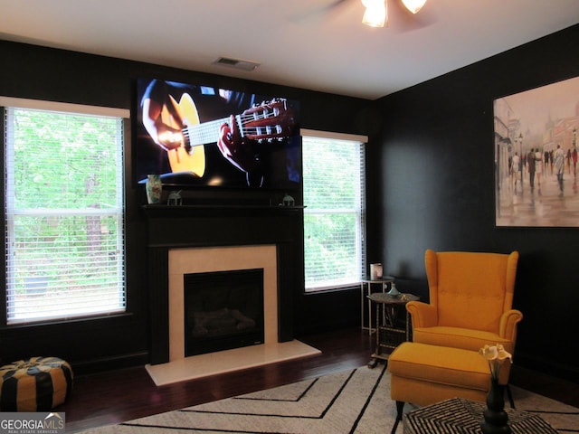 sitting room featuring ceiling fan, a fireplace with raised hearth, wood finished floors, and visible vents