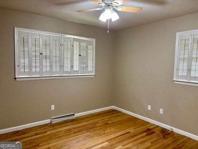 spare room with a baseboard radiator, visible vents, baseboards, wood finished floors, and a ceiling fan