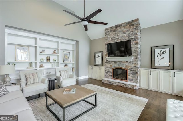 living area with high vaulted ceiling, a ceiling fan, a stone fireplace, and wood finished floors