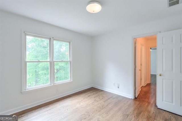 spare room with baseboards, a wealth of natural light, light wood-type flooring, and visible vents