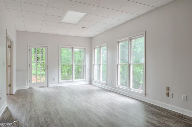 empty room featuring baseboards, a paneled ceiling, and wood finished floors