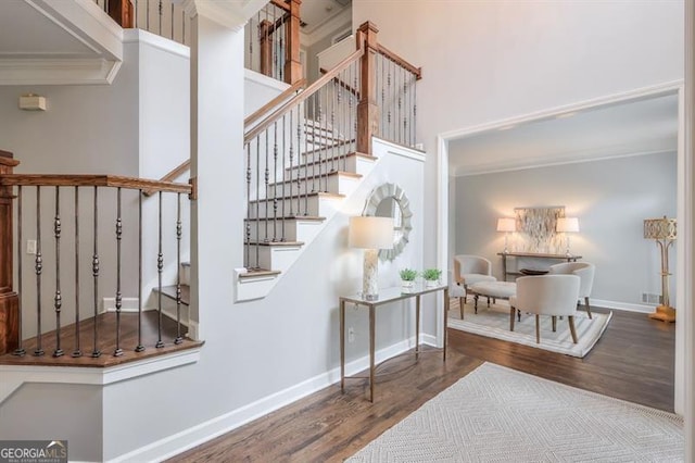stairway with crown molding, baseboards, wood finished floors, a towering ceiling, and visible vents