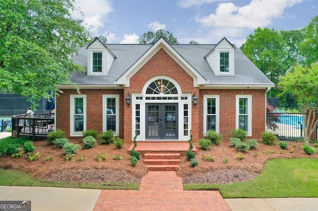 cape cod home featuring brick siding, fence, french doors, and a shingled roof