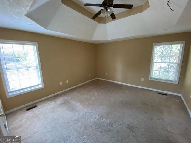 empty room featuring carpet, baseboards, visible vents, a raised ceiling, and a ceiling fan