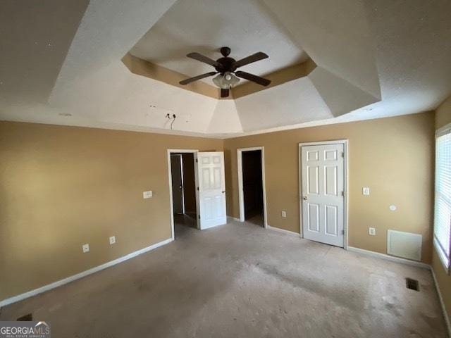 unfurnished bedroom with two closets, carpet, baseboards, visible vents, and a tray ceiling