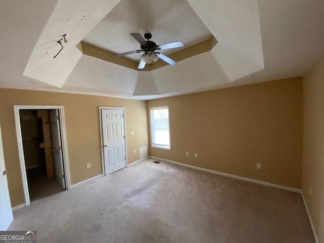 unfurnished bedroom with baseboards, light carpet, ensuite bathroom, and a tray ceiling