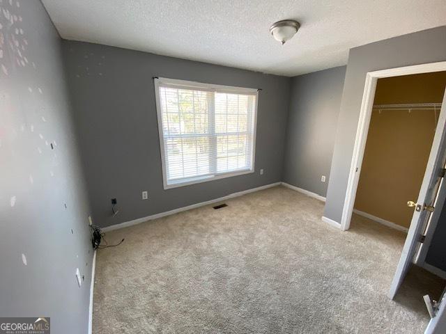 unfurnished bedroom featuring carpet floors, a closet, baseboards, visible vents, and a textured ceiling