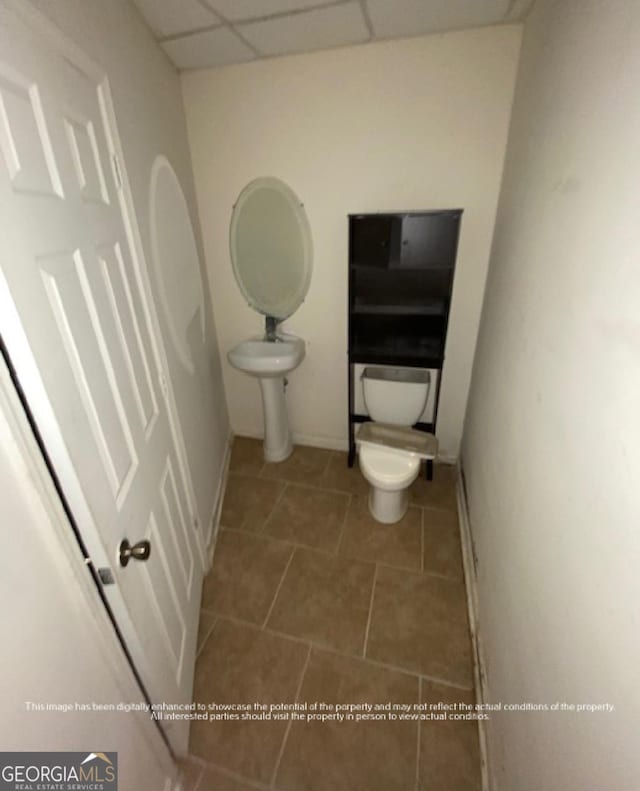 half bath featuring toilet, a drop ceiling, tile patterned floors, and baseboards