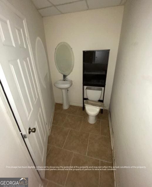 half bath with tile patterned floors, baseboards, toilet, and a drop ceiling