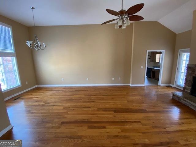 unfurnished living room featuring baseboards, high vaulted ceiling, wood finished floors, and ceiling fan with notable chandelier