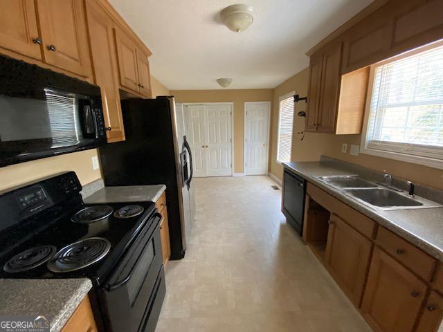 kitchen with baseboards, black appliances, light floors, and a sink