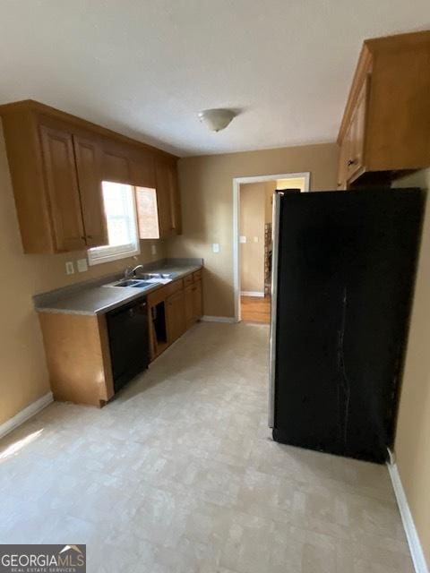 kitchen with brown cabinets, a sink, freestanding refrigerator, baseboards, and black dishwasher