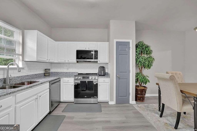 kitchen with light stone counters, appliances with stainless steel finishes, backsplash, a sink, and white cabinetry