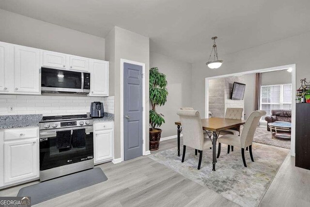 kitchen with light stone countertops, light wood-style flooring, decorative backsplash, appliances with stainless steel finishes, and white cabinetry