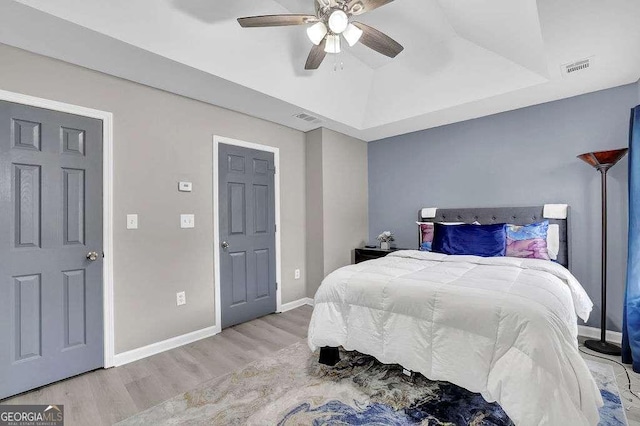 bedroom with a raised ceiling, visible vents, wood finished floors, and baseboards
