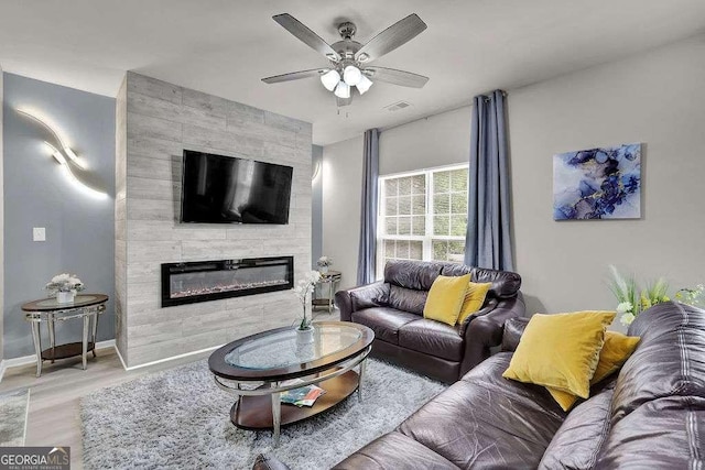 living area with a large fireplace, ceiling fan, visible vents, baseboards, and wood finished floors