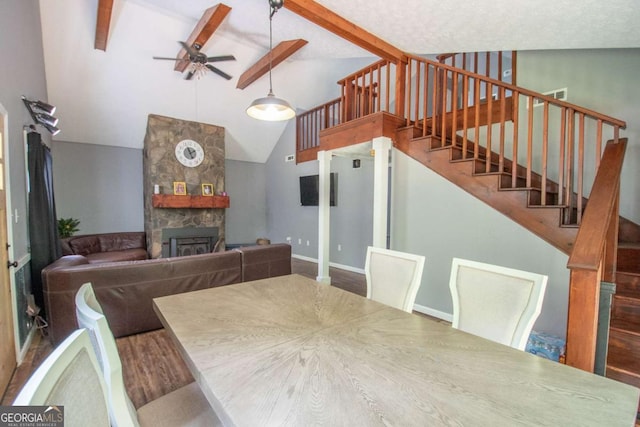 dining room featuring a fireplace, vaulted ceiling with beams, a ceiling fan, stairs, and baseboards