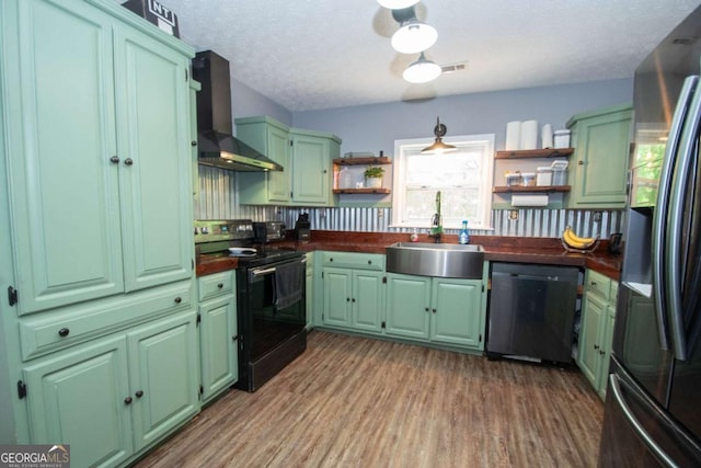 kitchen with a sink, green cabinets, open shelves, wall chimney range hood, and appliances with stainless steel finishes