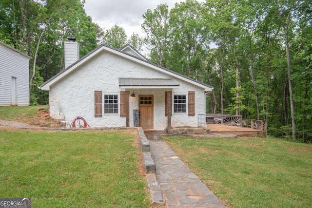 bungalow-style home with a chimney, a front yard, and a deck