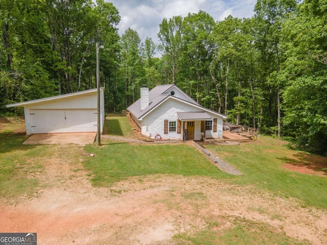view of front of home featuring a detached garage, a front lawn, a wooded view, and a chimney