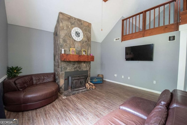 living area featuring visible vents, wood finished floors, high vaulted ceiling, and a stone fireplace
