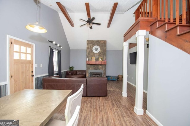 dining area featuring beamed ceiling, stairway, a ceiling fan, a stone fireplace, and wood finished floors