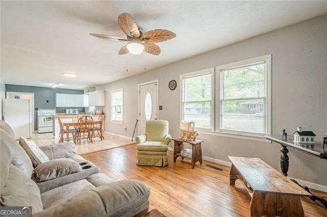 living room with ceiling fan, a textured wall, light wood finished floors, and baseboards