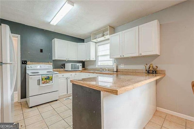 kitchen featuring white appliances, light tile patterned floors, a sink, white cabinetry, and a peninsula