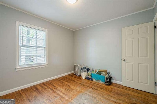 empty room featuring wood finished floors, crown molding, and baseboards