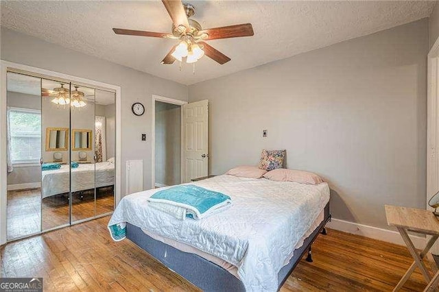 bedroom with a textured ceiling, ceiling fan, hardwood / wood-style floors, a closet, and baseboards