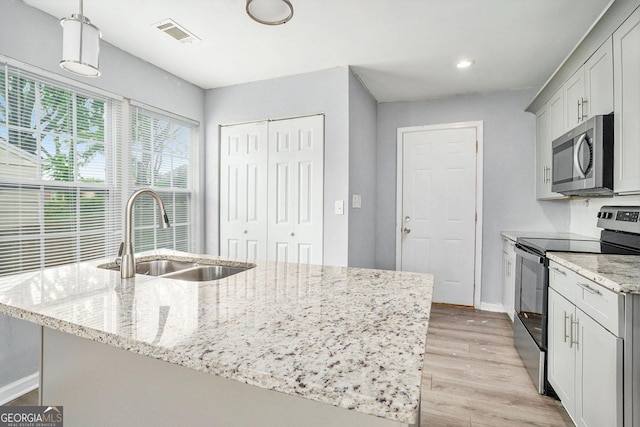 248 Upshaw St SW, Atlanta, GA 30315 - kitchen featuring appliances with stainless steel finishes, light wood-style flooring, light stone countertops, a center island with sink, and pendant lighting