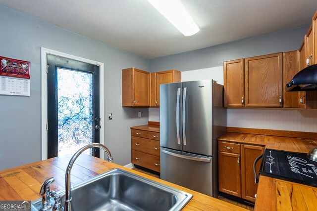 kitchen featuring freestanding refrigerator, a sink, butcher block counters, and brown cabinets