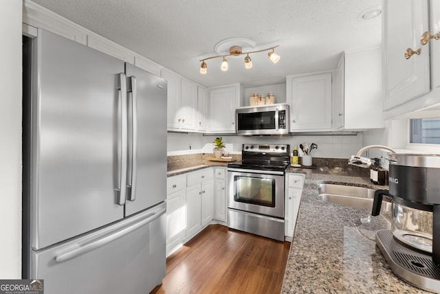 kitchen featuring white cabinetry, appliances with stainless steel finishes, a sink, and dark stone countertops