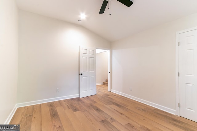 empty room featuring baseboards, ceiling fan, light wood-style floors, and vaulted ceiling