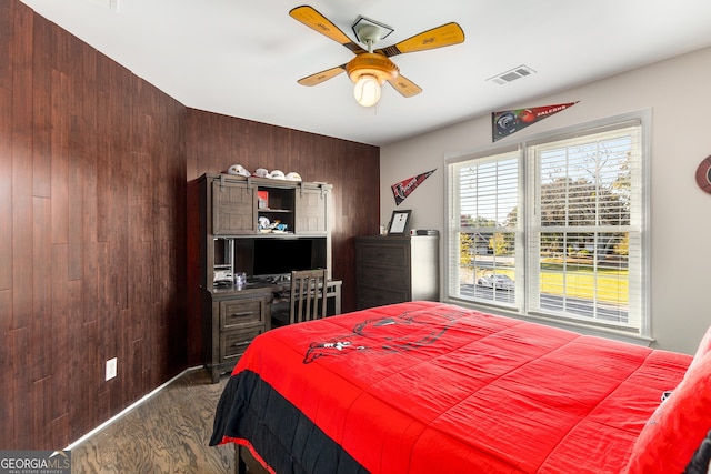bedroom featuring visible vents, wood walls, ceiling fan, and dark wood-style floors