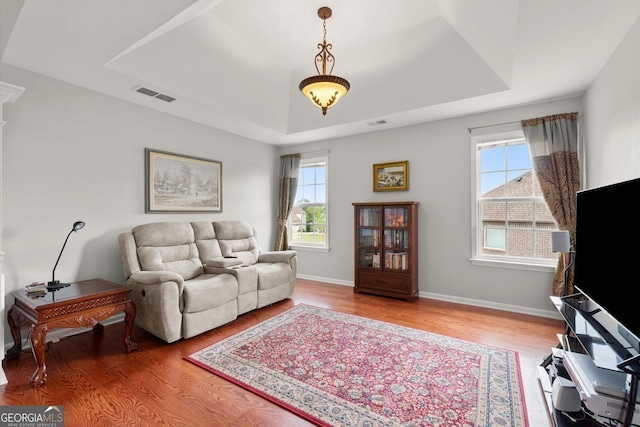 living area featuring a healthy amount of sunlight, a raised ceiling, wood finished floors, and visible vents
