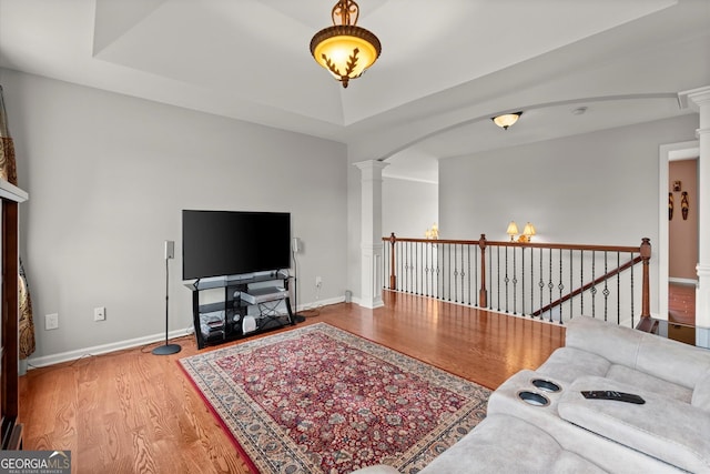 living area featuring baseboards, decorative columns, arched walkways, and wood finished floors